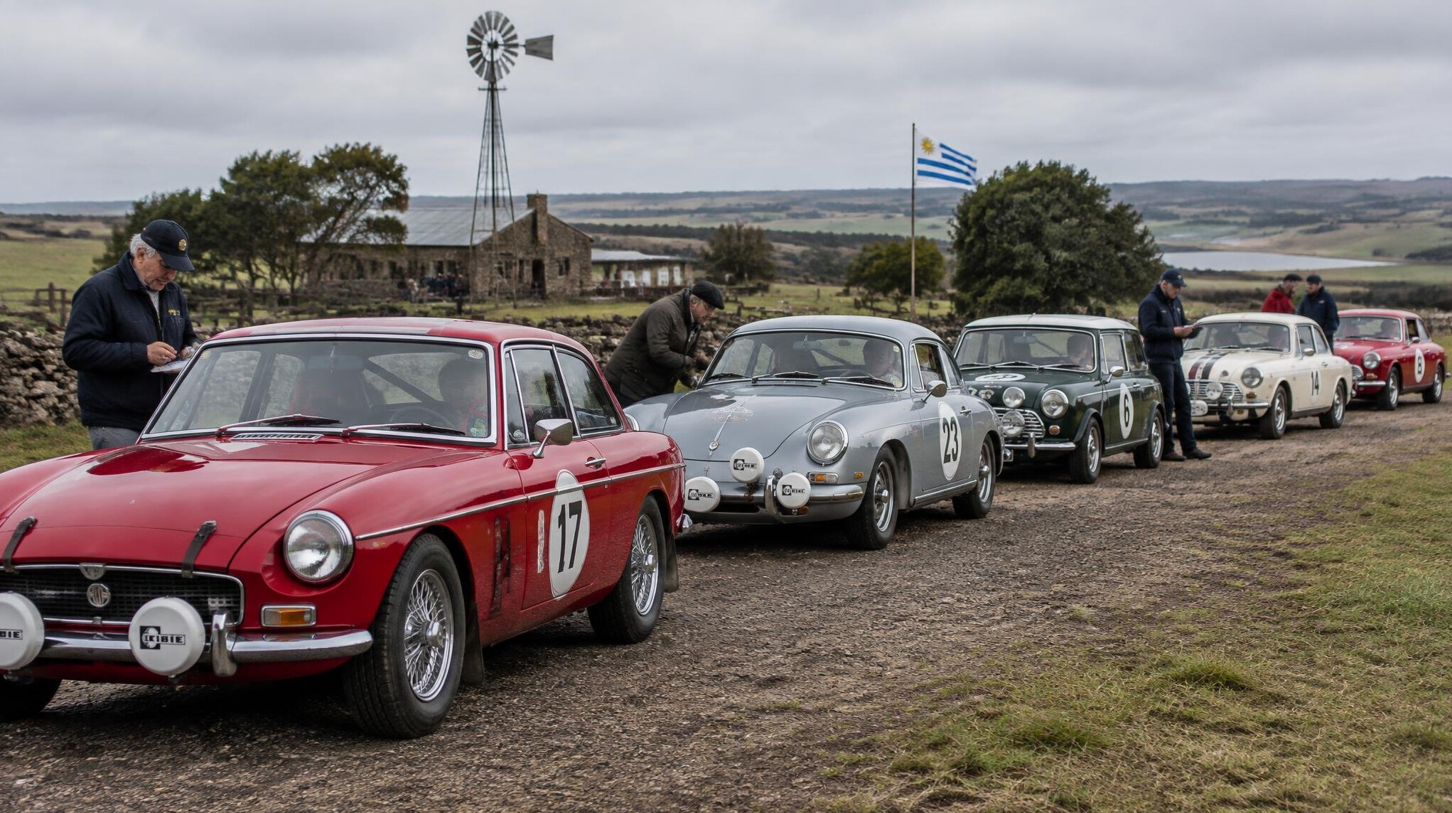 A row of classic rally cars lined up before a vintage automobile rally in the countryside